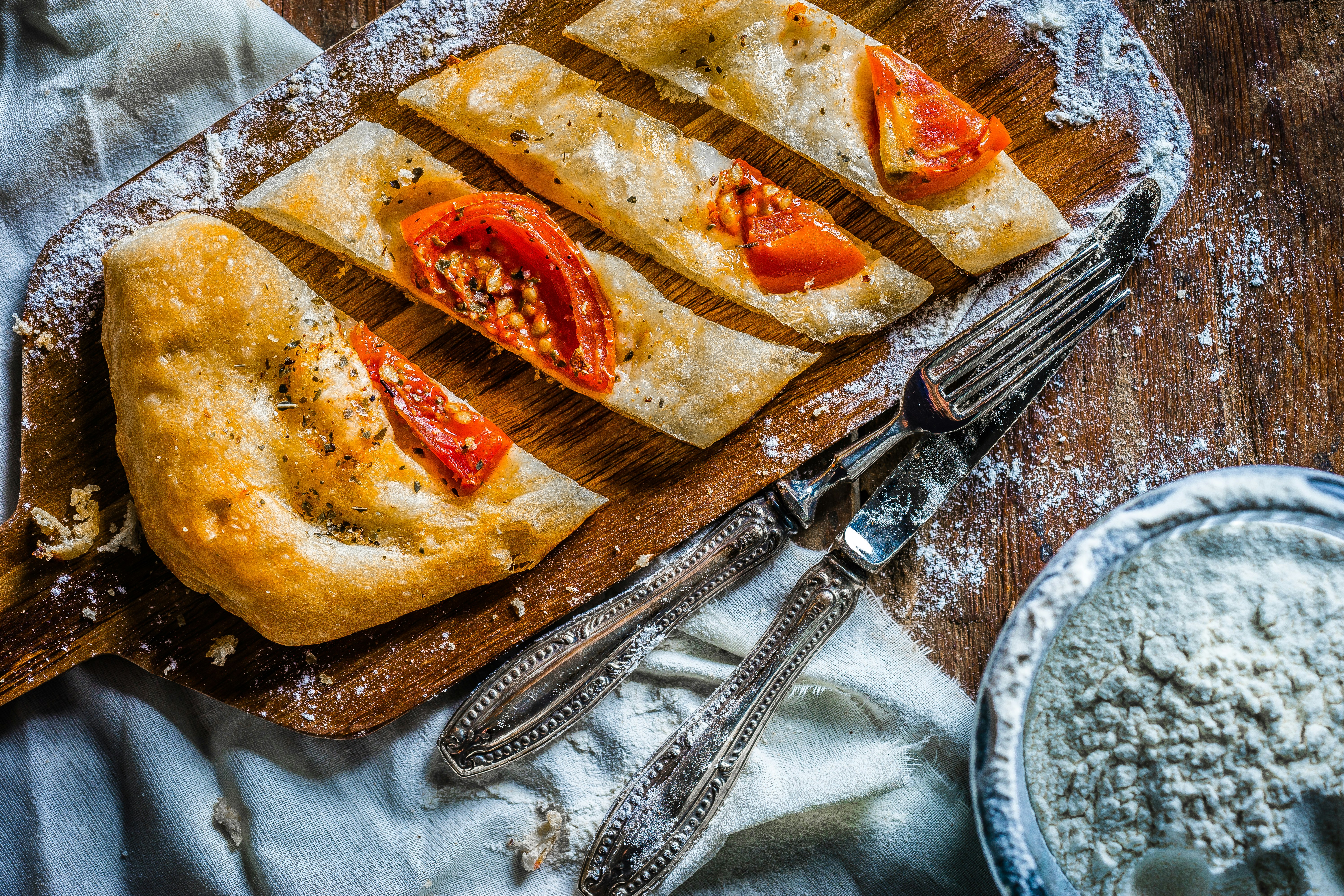 photo of bread with tomato on wooden board beside spoon and knife